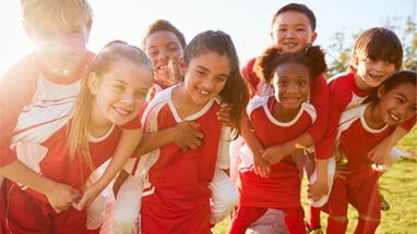 Kinder in roten Sporttrikots lächeln im Freien bei Sonnenuntergang.
