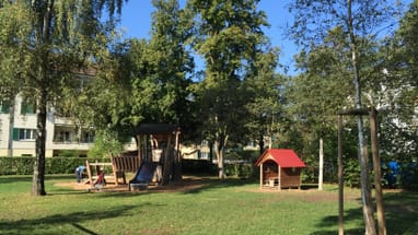Spielplatz mit Rutsche und Holzhütten im Park.