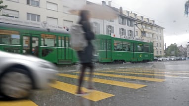 Person bei Regen auf Zebrastreifen, grüner Strassenbahn im Hintergrund."  