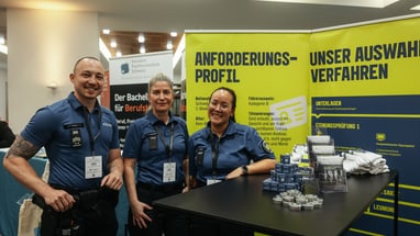 Die Resortleitung und eine Mitarbeiterin der Rekrutierung stehen an einem Infostand.