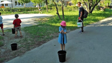 Kinder spielen draussen mit Eimern auf einem Weg.",