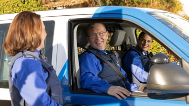 Zwei Personen sitzen in einem Polizeiauto des Verkehrsdienst und begrüssen eine Kollegin