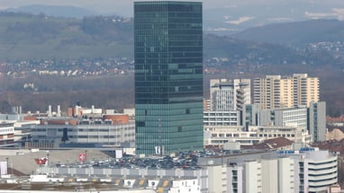 Stadtbild mit hohem Glasgebäude und umliegenden Gebäuden.