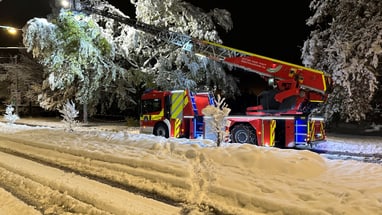 Feuerwehrfahrzeug mit Leiter im verschneiten Nachtwald.",