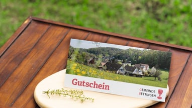 Gutschein auf Tisch im Freien mit grüner Wiese im Hintergrund.