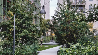 Gehweg zwischen modernen Gebäuden und grünen Bäumen.