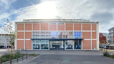 Backsteingebäude mit Glasfront unter sonnigem Himmel.