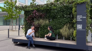 Zwei Personen sitzen vor einer bepflanzten Struktur in der Stadt Basel.