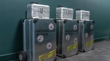 Drei Archäologiekoffer vor grünem Hintergrund.