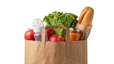 Papiertüte mit Äpfeln, Salat, Brot und Flasche.