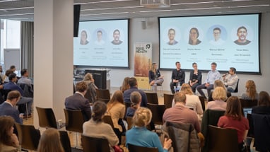 Paneldiskussion vor Publikum mit Moderator und Rednern auf Bühne.