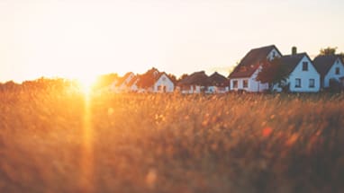 Häuserreihe in ländlicher Landschaft bei Sonnenuntergang.