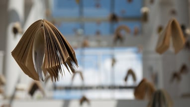 Schwebende Bücher vor Glasdecke in modernem Gebäude.