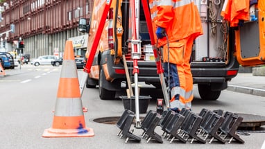 Arbeiter in orange Kleidung arbeiten an einem offenen Gully auf der Strasse.