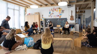 Gruppe von Menschen, die in einem Kinderzimmer im Kreis sitzen.
