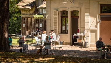 Leute sitzen draussen im Café unter Bäumen.