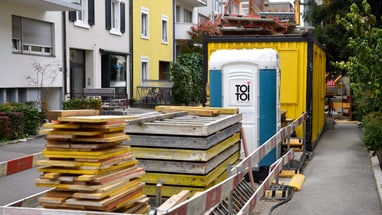 Bauarbeiten auf der Strasse mit Baumaterialien und mobilen Toiletten.