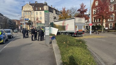 Strassenszene mit Polizeipräsenz neben einem Lastwagen und Wohnhäusern im Hintergrund.