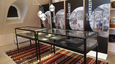 Museumsvitrine mit Exponaten vor Informationstafeln zur Bronze-, Eisen- und Römerzeit.