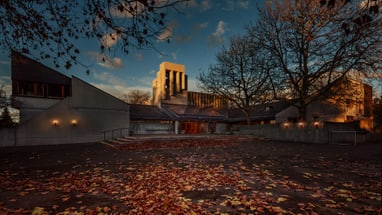 Kirchengebäude im Abendlicht mit Laub im Vordergrund.