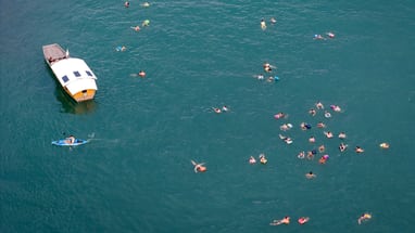 Menschen schwimmen neben einem Boot im Wasser.