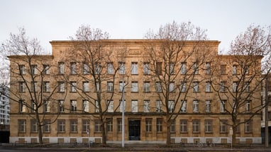 Historisches Gebäude mit Bäumen an der Strasse.",