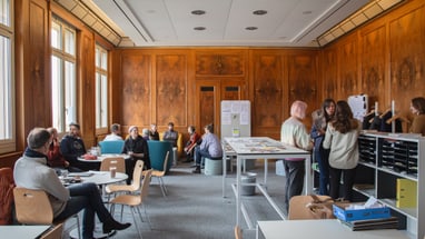 Personen in einem Raum mit Holzwänden arbeiten in Gruppen zusammen.
