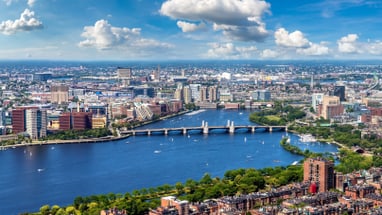 Stadtansicht mit Fluss und Brücke unter blauem Himmel.