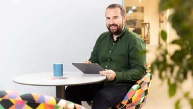 Mann mit Tablet am runden Tisch lächelnd.