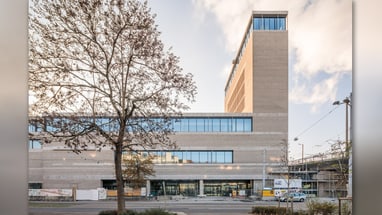 Moderne mehrstöckige Backsteinfassade mit Baum im Vordergrund.