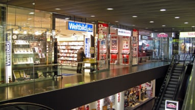 Person beim Betreten eines Geschäfts im Einkaufszentrum neben einer Rolltreppe.