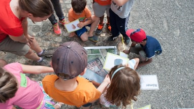 Gruppe von Kindern schaut auf Bilder auf dem Boden draussen sitzend.