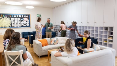 Menschen in einem Gemeinschaftsraum mit Sofas und Wanddekoration.