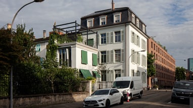 Wohngebäude mit Autos auf der Strasse, bepflanzter Balkon.