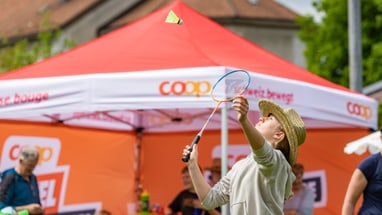 Person spielt Federball vor einem roten Zelt im Freien.