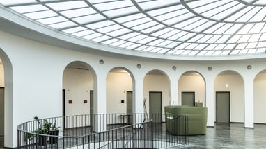 Runder Raum mit Glasdach und Treppe in der Mitte.