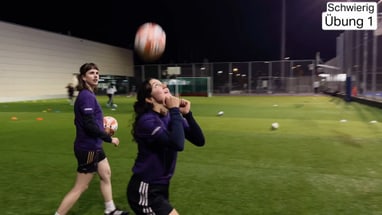 Zwei Personen spielen auf einem Fussballplatz bei Nacht, Konzentration auf den Ball.",