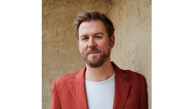 Mann in roter Jacke steht vor einer Wand.