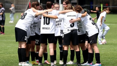 Mädchenfussballmannschaft bildet einen Kreis auf dem Spielfeld.