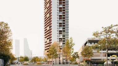 Hochhaus an einer leeren Strasse mit Bäumen bei Tageslicht.