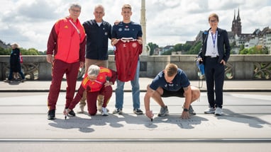 Gruppe von Personen auf einer Brücke, zwei knien und schreiben auf den Boden.