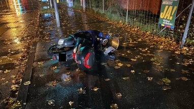 Umgestürztes Motorrad auf nasser Strasse bei Nacht mit Herbstlaub.",