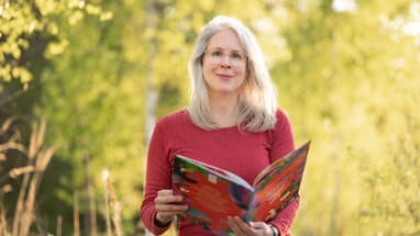 Frau mit langen Haaren liest ein Buch im Freien.