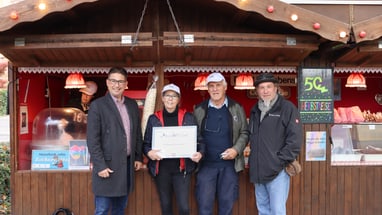 Menschen vor Süssigkeitenstand mit Zertifikat in der Hand.