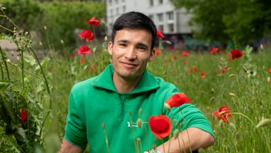 Lernender Mann sitzt zwischen roten Blumen.