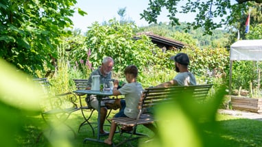 Drei Personen sitzen an einem Tisch im Garten.
