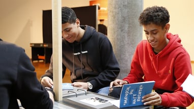 Zwei Jugendlich lesen Broschüren und diskutieren an einem Tisch.