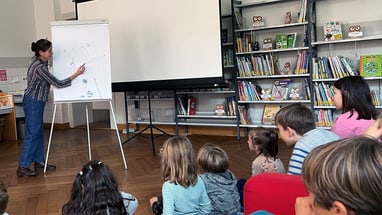 Autorin Verena Pavoni zeichnet vor einer Gruppe von Kindern auf einem Flipchart in der Bibliothek.