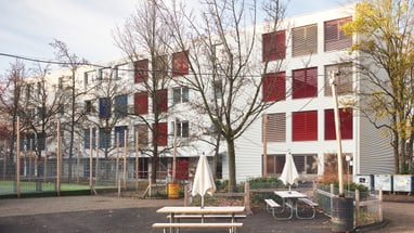 Moderner Schulgebäude mit Bäumen und Tisch im Vordergrund.