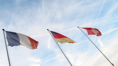 Französische, deutsche und schweizer Flaggen wehen gegen einen blauen Himmel.